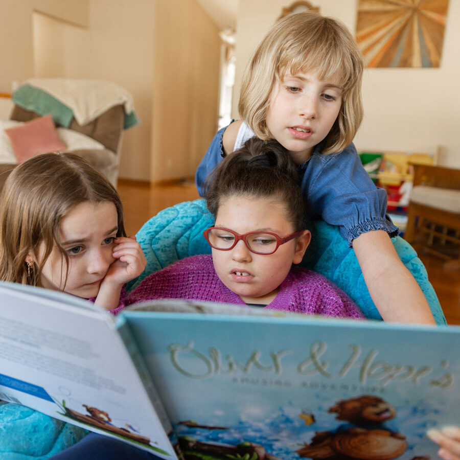 Three little girls sit together reading an Oliver & Hope picture book.