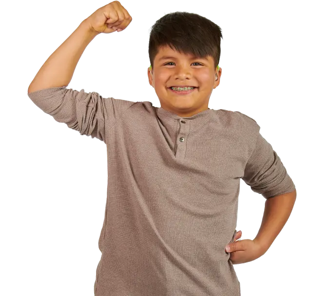 A little boy named Noah with braces from Thornton, CO smiles at the camera with one fist on his hip and the other arm flexing his muscles.