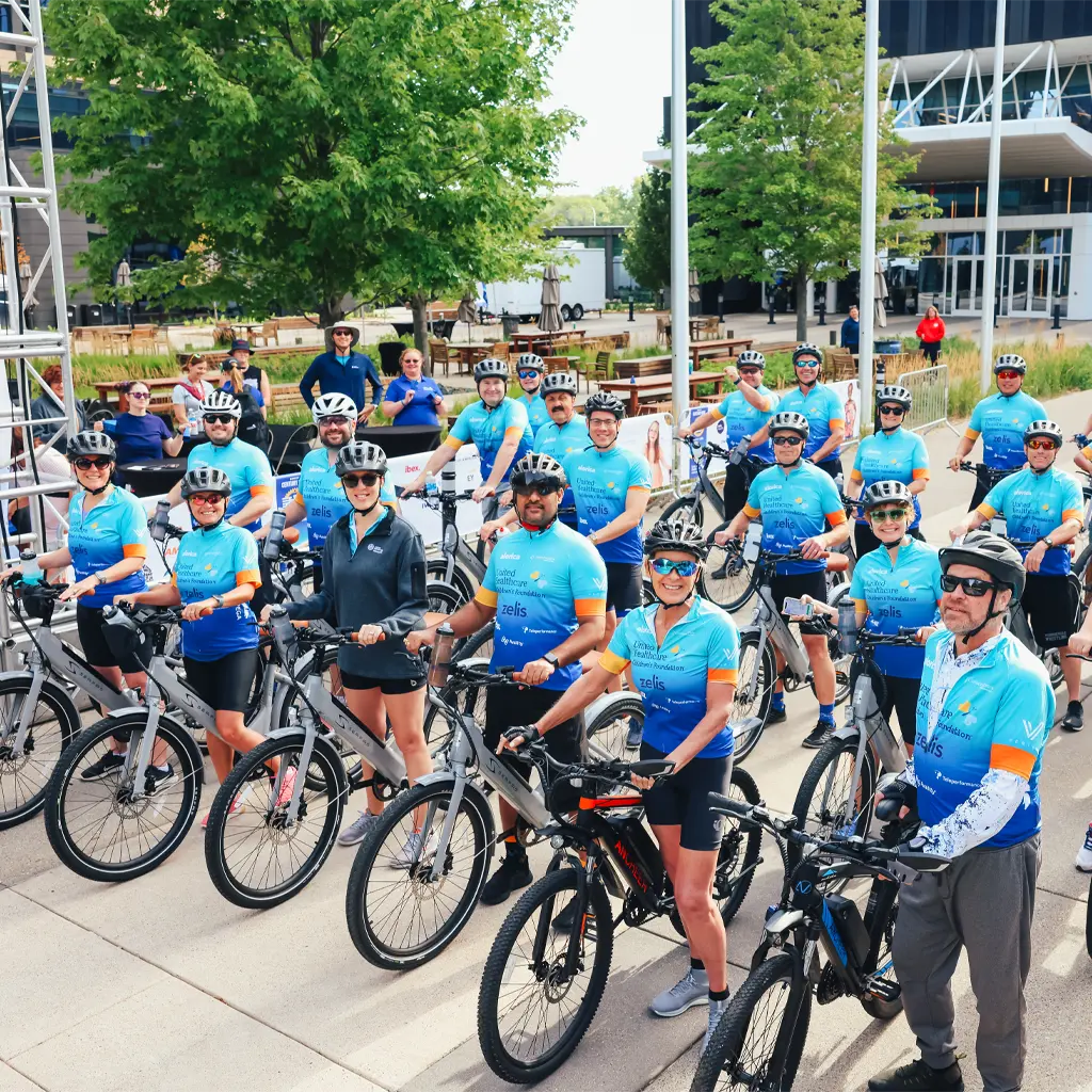 A group of people in Minnesota Century Ride event shirts and helmets stand next to their bikes and smile at the camera.