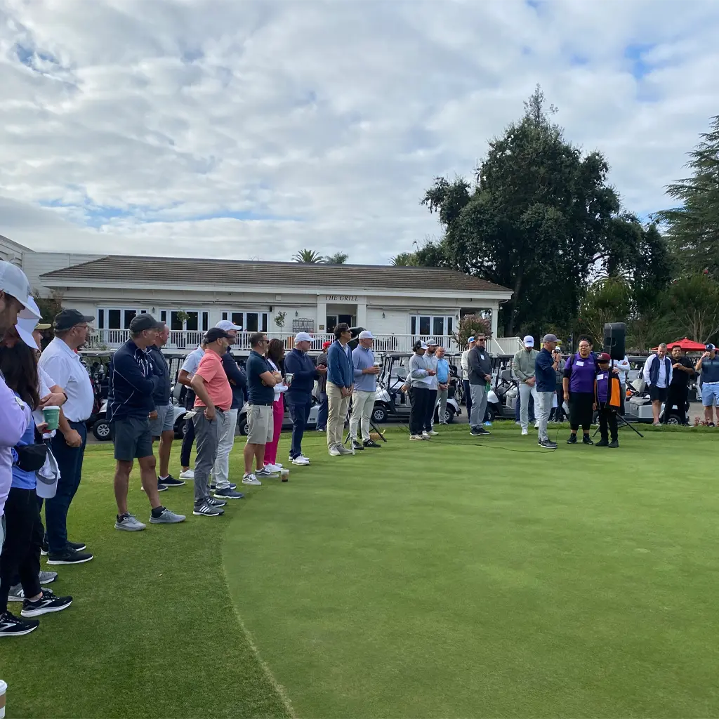 A large group of people stand on the green at a California Golf + Wine event.