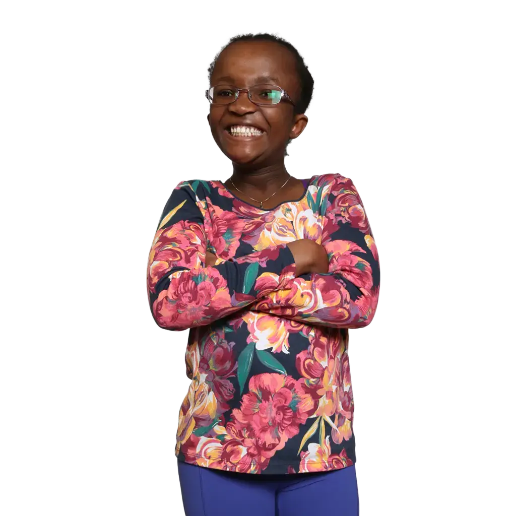 A little girl in glasses named Naomi smiles widely at the camera with her arms crossed.