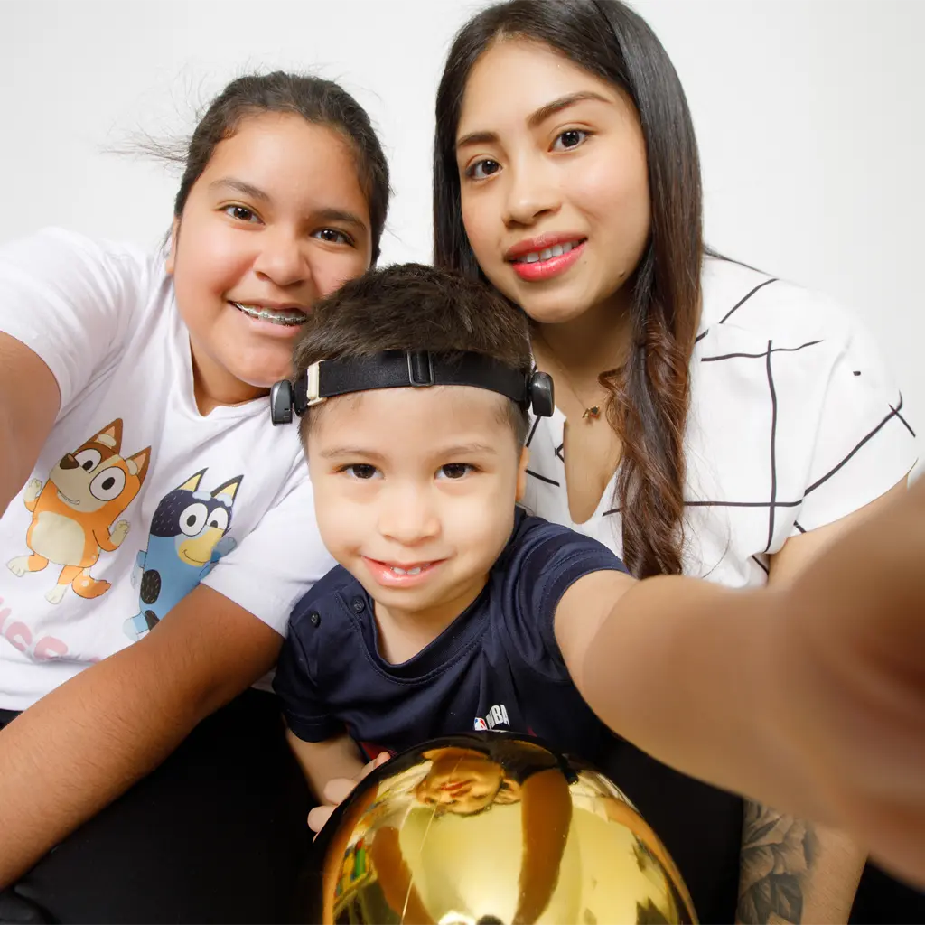 A little boy named Adrian takes a selfie with his mom and sister while holding a gold ball.